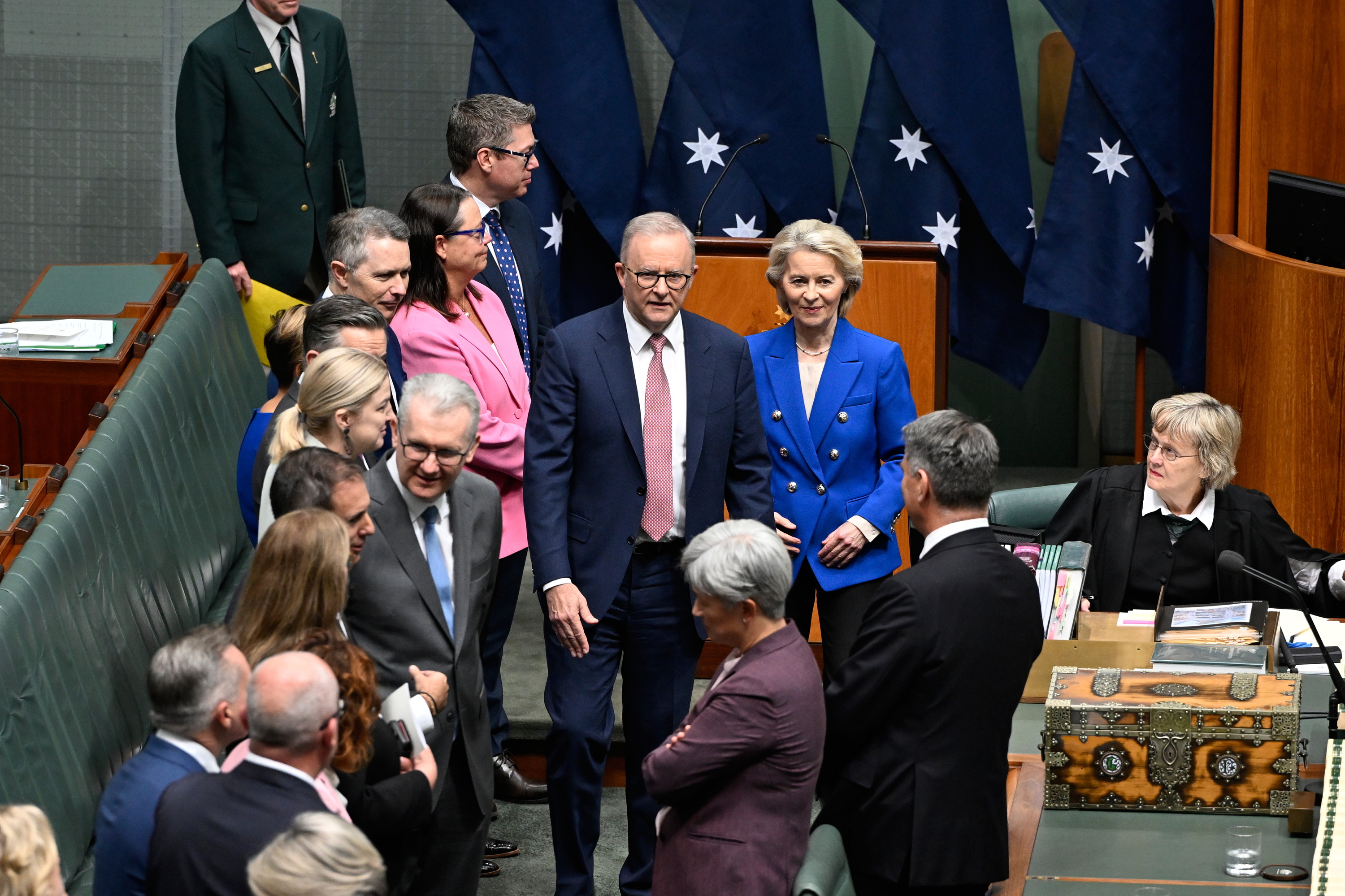 A group of people, including Prime Minister Anthony Albanese in a suit and President von der Leyen in a blue blazer, stand and speak with Members and Senators on the floor of the House of Representatives.