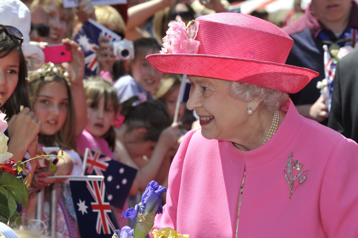 Her Majesty The Queen wearing a pink hat and jacket as she greets a crowd