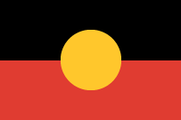 Image of a flag. The top half of the flag is black. The lower half is red. There is a circle of yellow in the centre of the flag.
