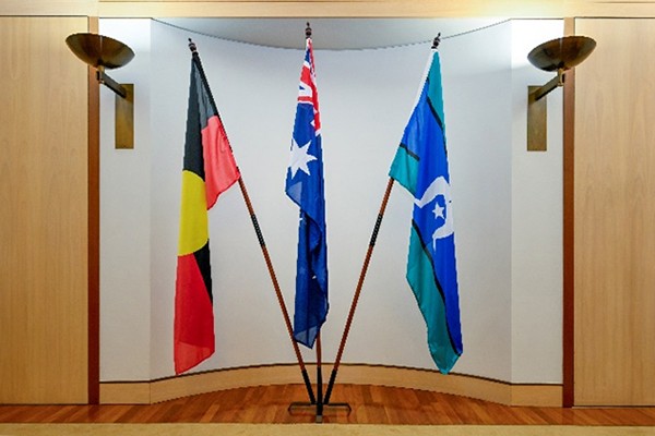 Three flagpoles in a stand with the middle one taller and the others at an angle.