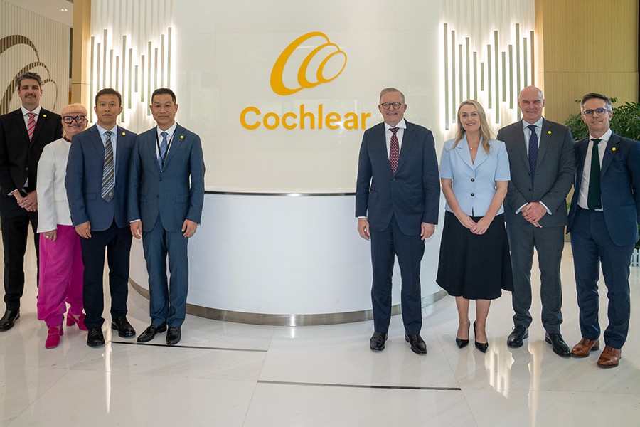 Prime Minister Anthony Albanese with partner, Jodie Haydon, standing alongside other officials in front of Cochlear Australia sign.