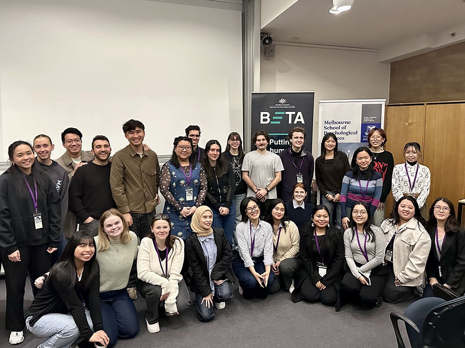 Several university students pose for a group photo in front of a BETA and University of Melbourne banner.