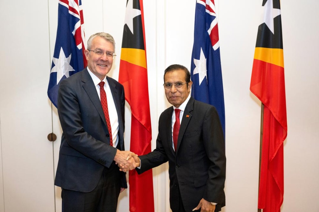 The Hon Mark Dreyfus KC MP and Prime Minister Taur Matan Ruak shake hands in front of the flags of both nations