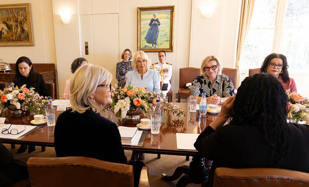 Her Majesty sits in conversation at a long table with a group of women.