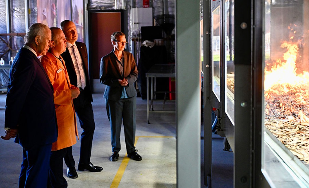 His Majesty stands with a small group watching a simulated bushfire behind toughened glass viewing doors.
