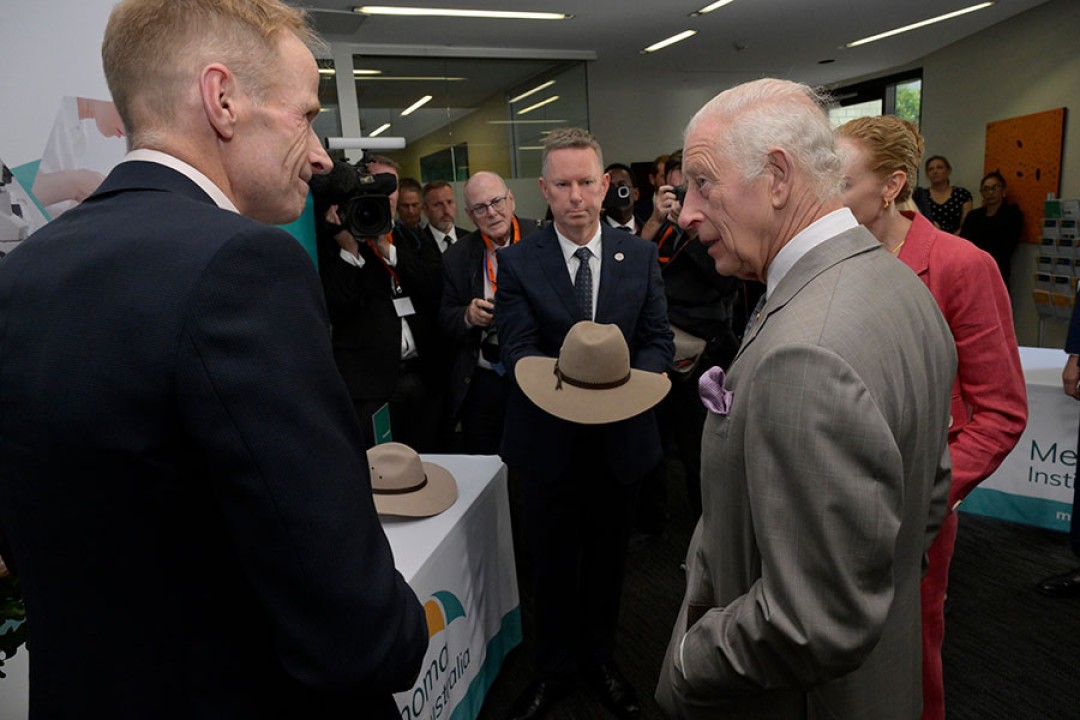 His Majesty engages in conversation in front of tables with banners promoting the Melanoma Institute of Australia.