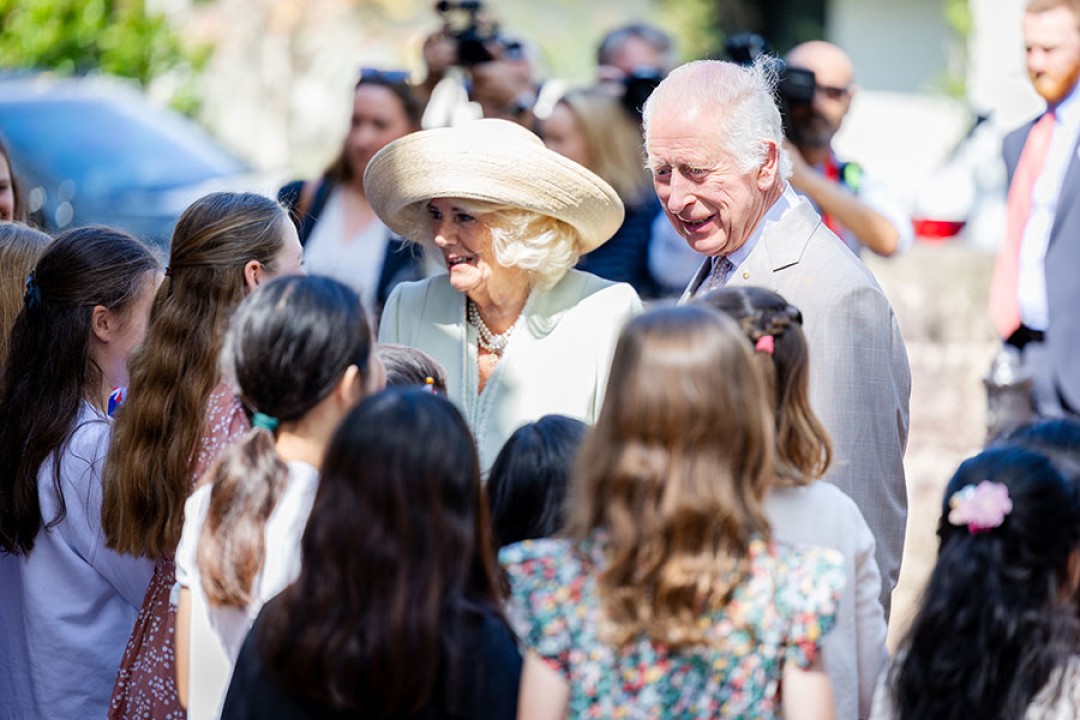 Their Majesties greeting a crowd of young girls with photographers looking on.