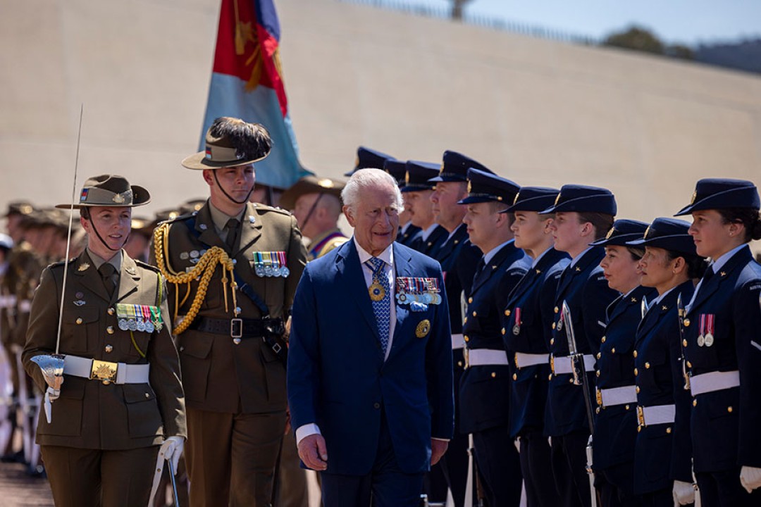 His Majesty walks in front of uniformed members of the Australian Federation Guard, escorted by two officers.