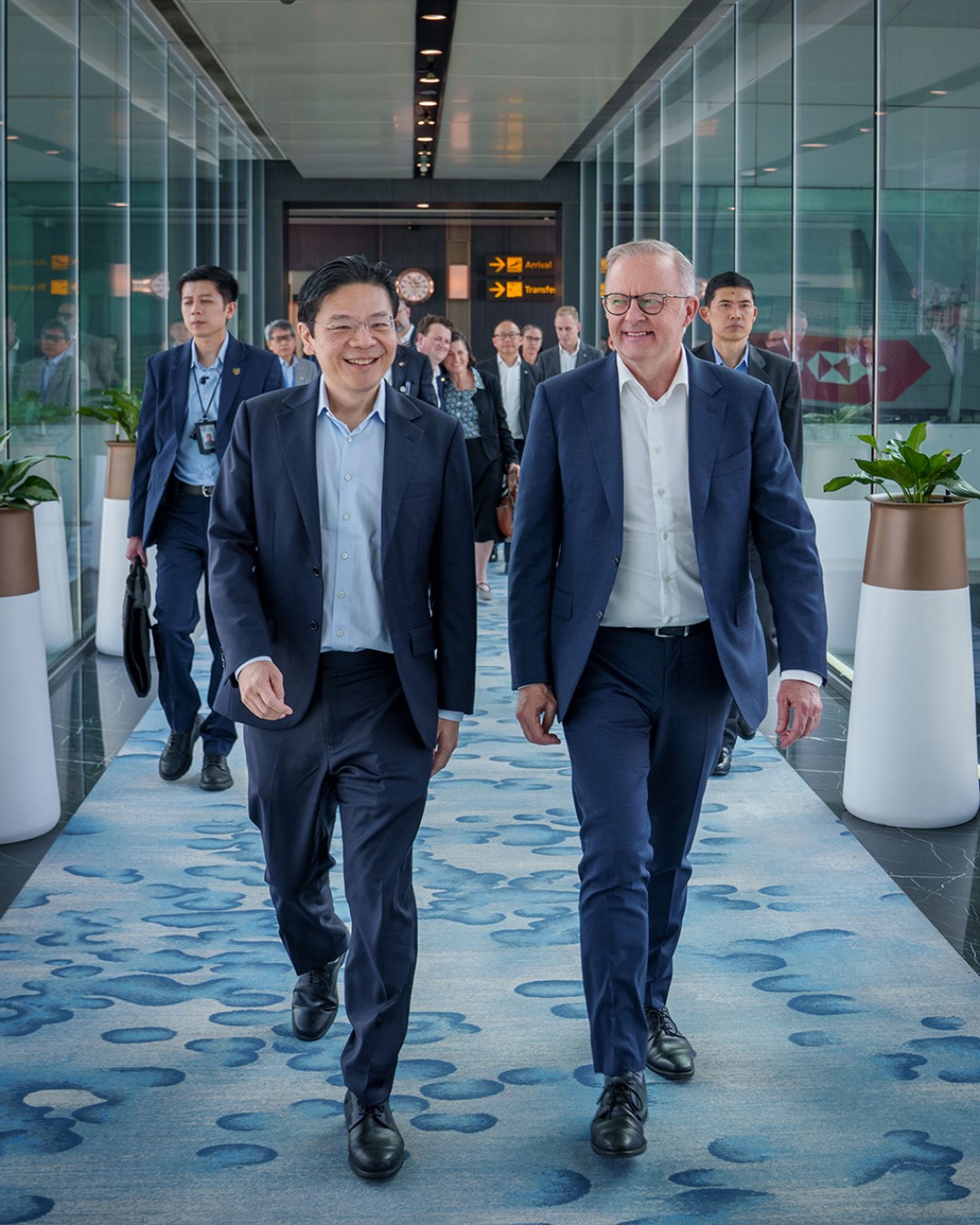 Prime Minister Anthony Albanese with Prime Minister Lawrence Wong in Singapore. They walk down a corridor followed by people.