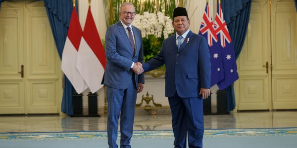 Prime Minister Anthony Albanese shakes hands with Indonesian President Prabowo Subianto in Jakarta in front of the flags of Indonesia and Australia.