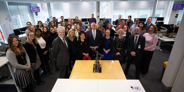 Professor Glyn Davis AC with approximately 40 PM&C staff surrounding former Governor-General Sir Peter Cosgrove in front of the Great Seal of Australia on a table.
