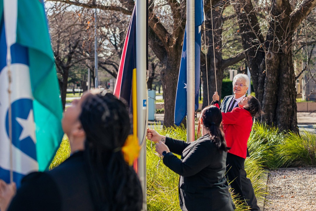 Professor Glyn Davis AC with 3 PM&C staff at flagpoles raising the Australian Aboriginal Flag, Torres Strait Islander Flag and the Australian National Flag.