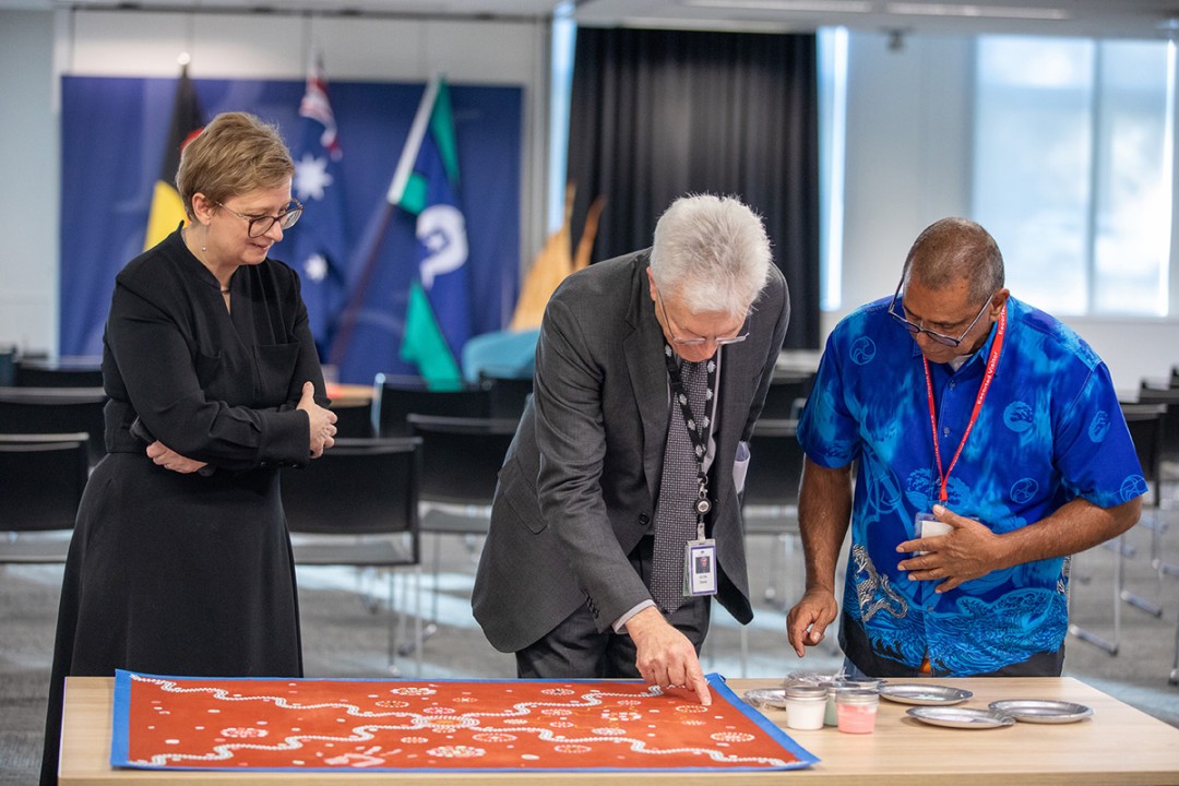 Professor Glyn Davis AC, James Baban, and another person looking down at James' artwork.