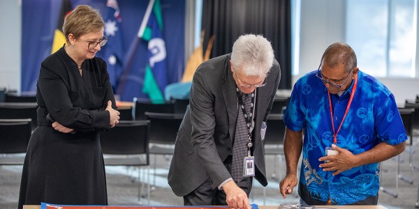 Professor Glyn Davis AC, James Baban, and another person looking down at James' artwork.