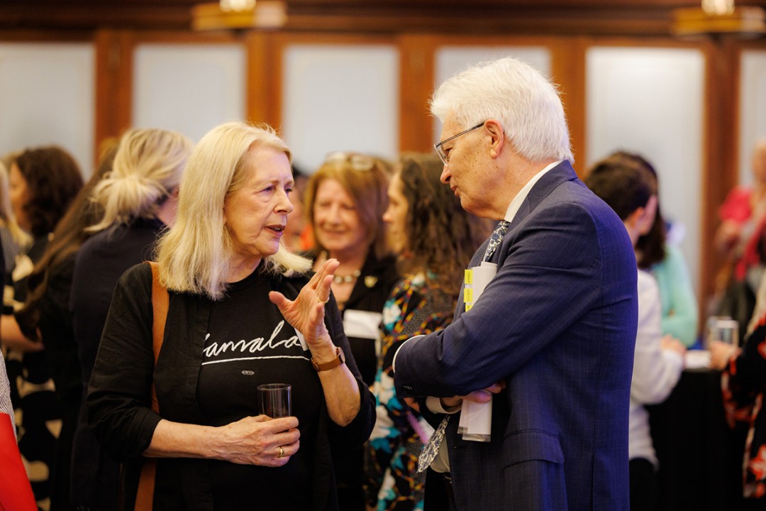 Dr Anne Summers AO talking with Professor Glyn Davis AC in front of a large group of people in the background.