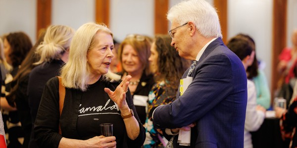 Dr Anne Summers AO talking with Professor Glyn Davis AC in front of a large group of people in the background.