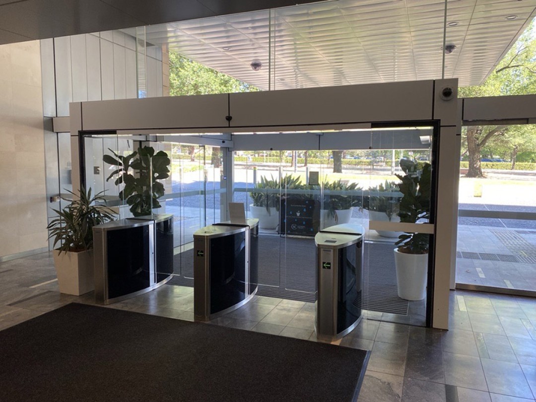 Shows glass automatic doors at the front entrance to the 1 National Circuit building leading out to the street side with a level walkway that has no obstructions.