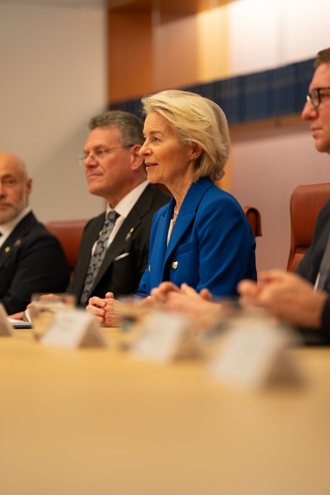President von der Leyen in a blue blazer sits at a conference table with several men in suits, smiling during a formal meeting.