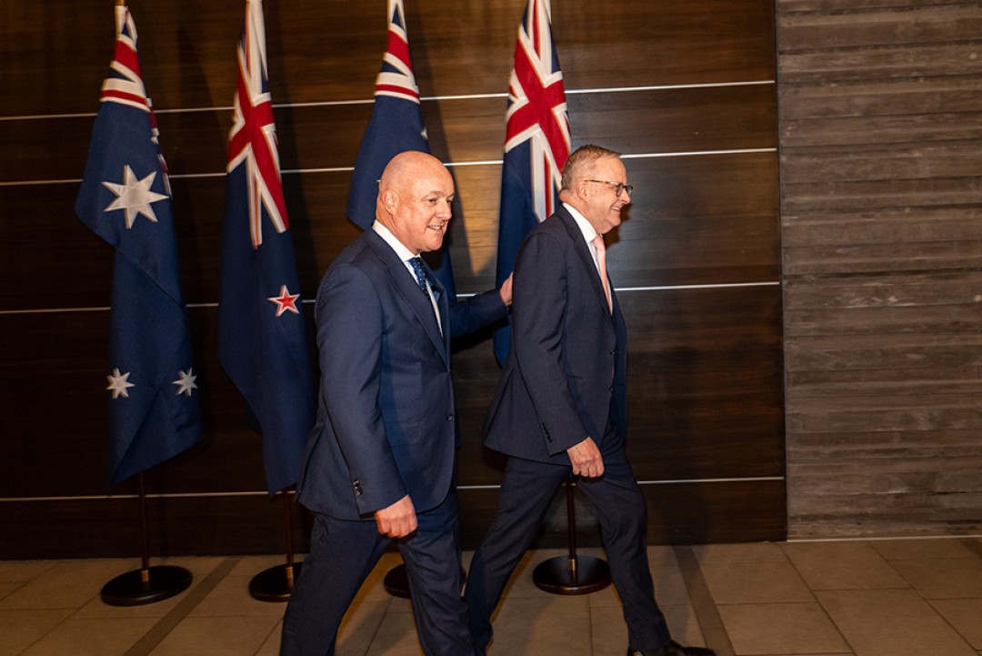 Prime Minister Anthony Albanese and New Zealand Prime Minister Christopher Luxon walking together past Australian and New Zealand flags.