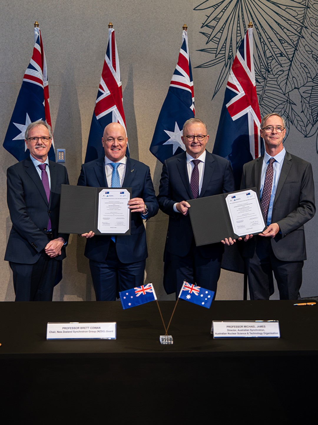 Prime Minister Anthony Albanese and New Zealand Prime Minister Christopher Luxon stand with representatives following a signing ceremony, holding signed documents.