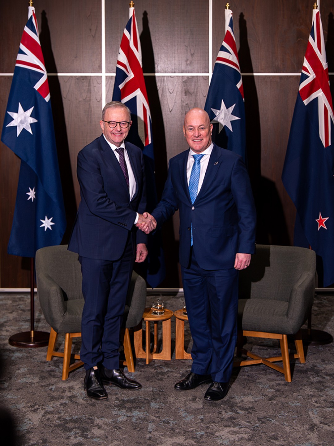 Prime Minister Anthony Albanese and New Zealand Prime Minister Christopher Luxon shake hands in front of Australian and New Zealand flags at the Australia–New Zealand Annual Leaders' Meeting.