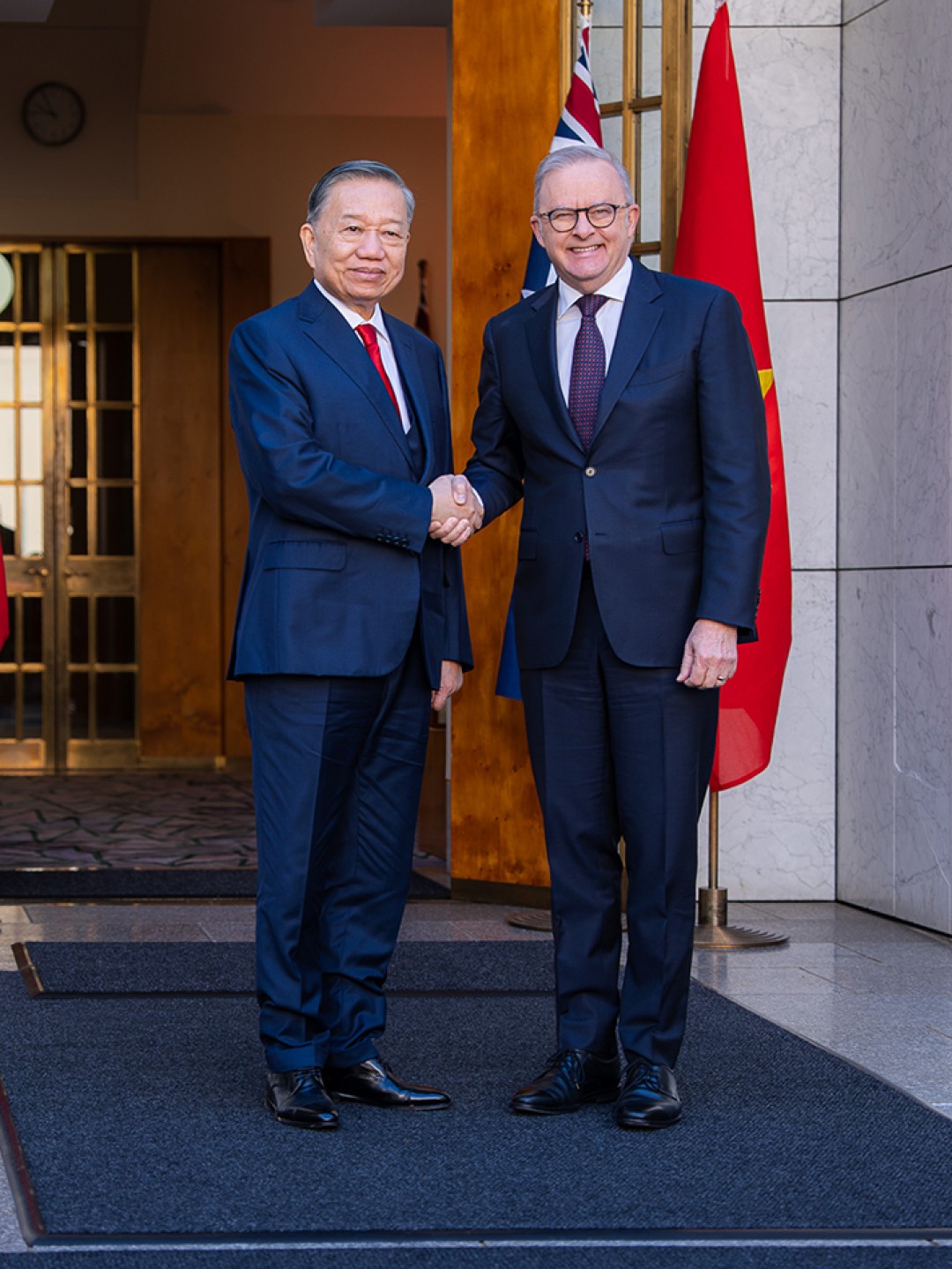 Prime Minister Anthony Albanese and General Secretary and President of the Socialist Republic of Vietnam To Lam shake hands at the entrance to Australian Parliament House, with Australian and Vietnamese flags behind them.