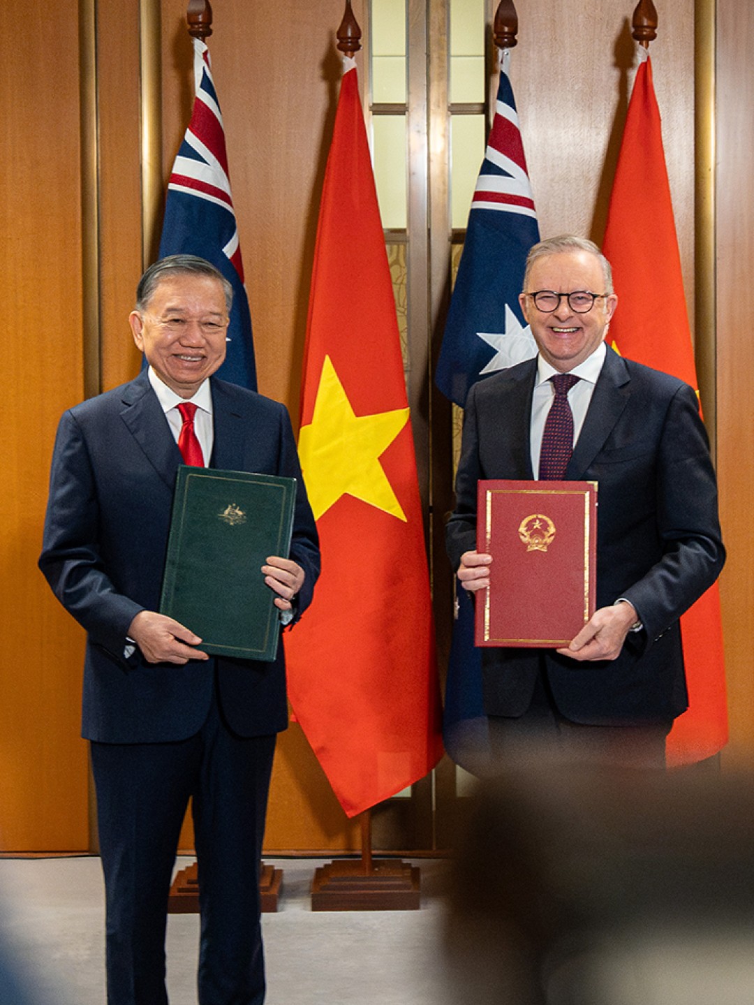 Prime Minister Anthony Albanese and General Secretary and President of the Socialist Republic of Vietnam To Lam hold signed documents during a ceremony at Australian Parliament House, with Australian and Vietnamese flags behind them.