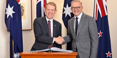 The Rt Hon Chris Hipkins and the Hon Anthony Albanese smile and shake hands in front of New Zealand and Australian flags