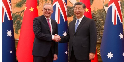 Australian Prime Minister Anthony Albanese is shaking hands with Chinese President Xi Jinping in front of Chinese and Australian flags in the background. 