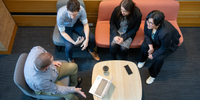 Four people dressed in business casual sit on couches around a coffee table