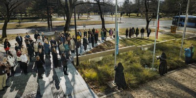 A group of people stand at the flagpoles for the Welcome to Country and flag raising ceremony at PM&C during NAIDOC Week in 2025.